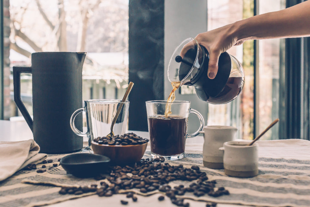 Hot coffee being poured surrounded by coffee beans
